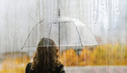 A woman silhouette with transparent umbrella through wet window with drops of rain. Autumn