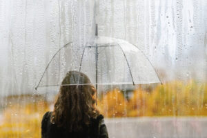 A woman silhouette with transparent umbrella through wet window with drops of rain. Autumn