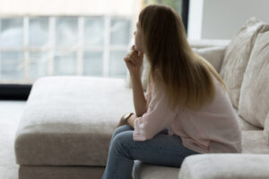 Lonely woman sitting on couch in living room, looking away